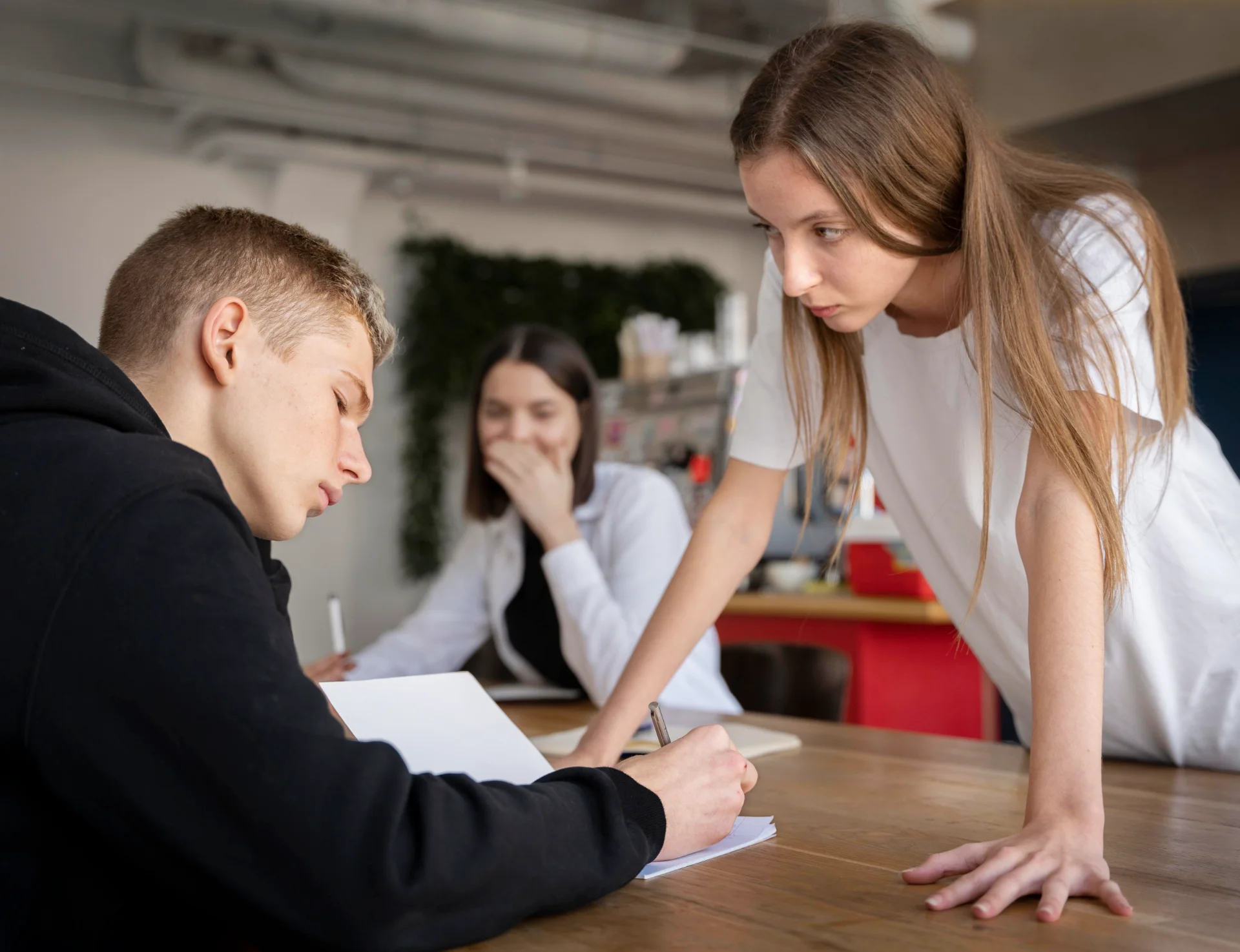 Ein Junge sitzt am Tisch und liest. Vor ihm steht ein Mädchen und beugt sich agressiv vor. Er bleibt aber ruhig.