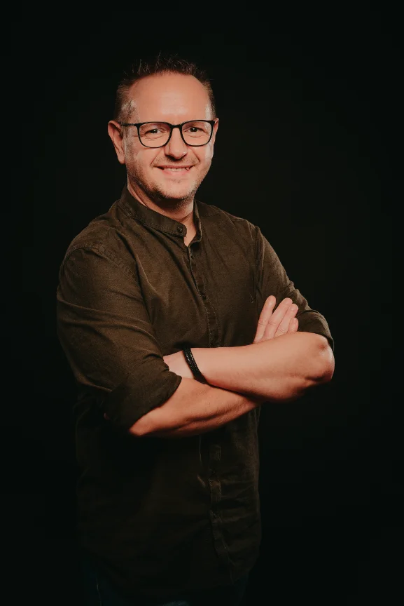 Portrait von Heiko Petersen stehend, die Arme verschränkt. Dunkler Hintergrund.